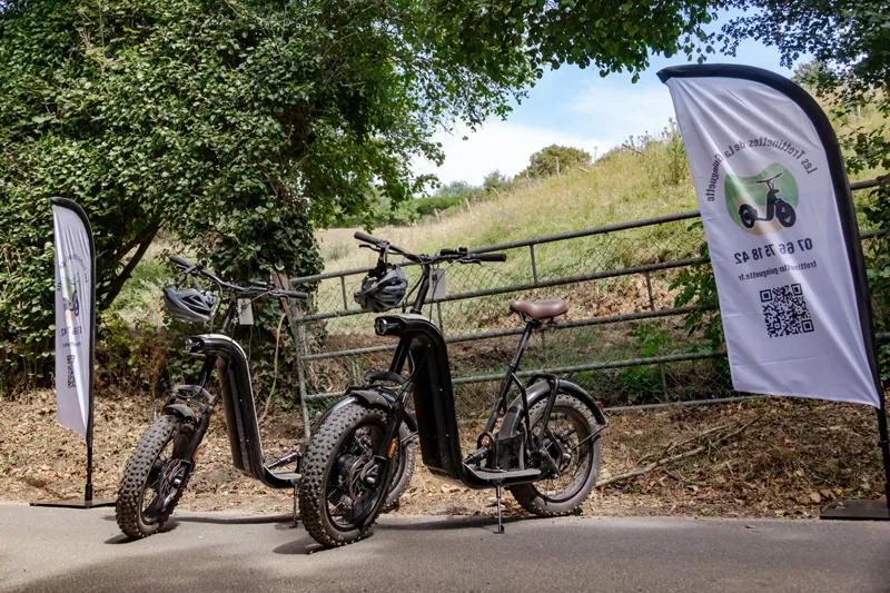 Deux trottinettes électriques tout-terrain prêtes pour le départ devant les oriflammes à l'entrée du circuit à Bellême.