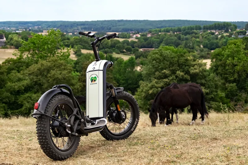Zoom sur une trottinette électrique tout-terrain de la marque française Zosh face aux paysages vallonnés du Perche.