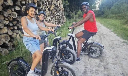 Trois participants en pleine randonnée guidée en trottinette tout-terrain sur un chemin de terre en forêt.